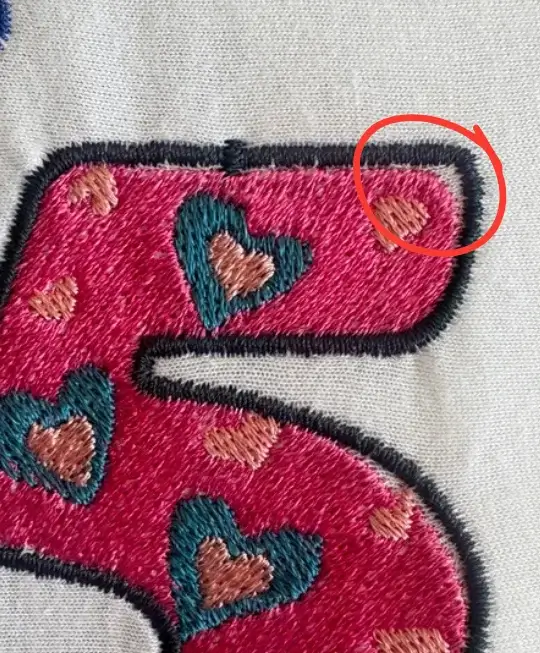 Close-up of stitched lettering showing a small corner gap where fabric pull, stitch angle, or weak underlay may affect the final sew-out.